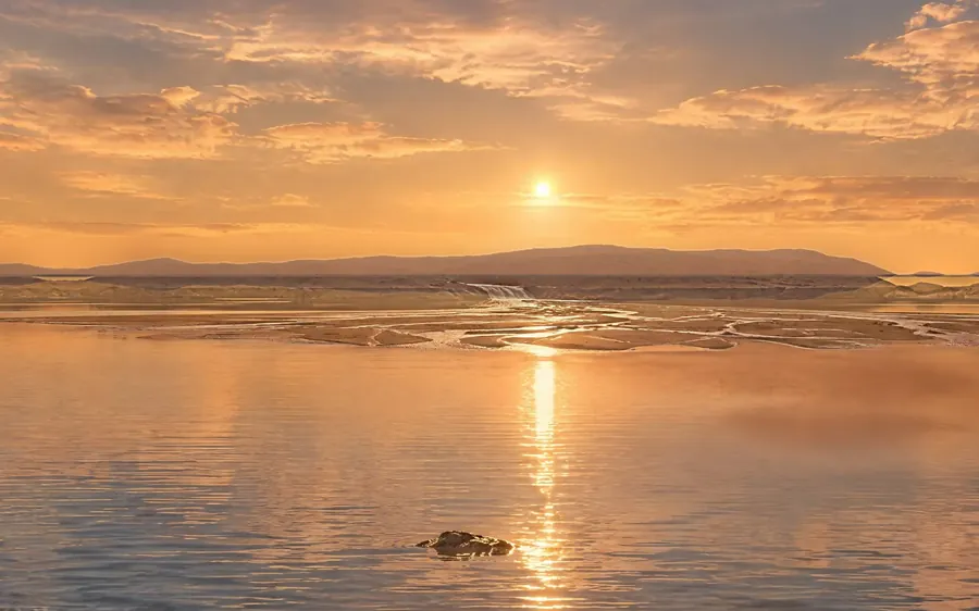 Sunset over a calm lake inside a crater, with a river delta in the distance